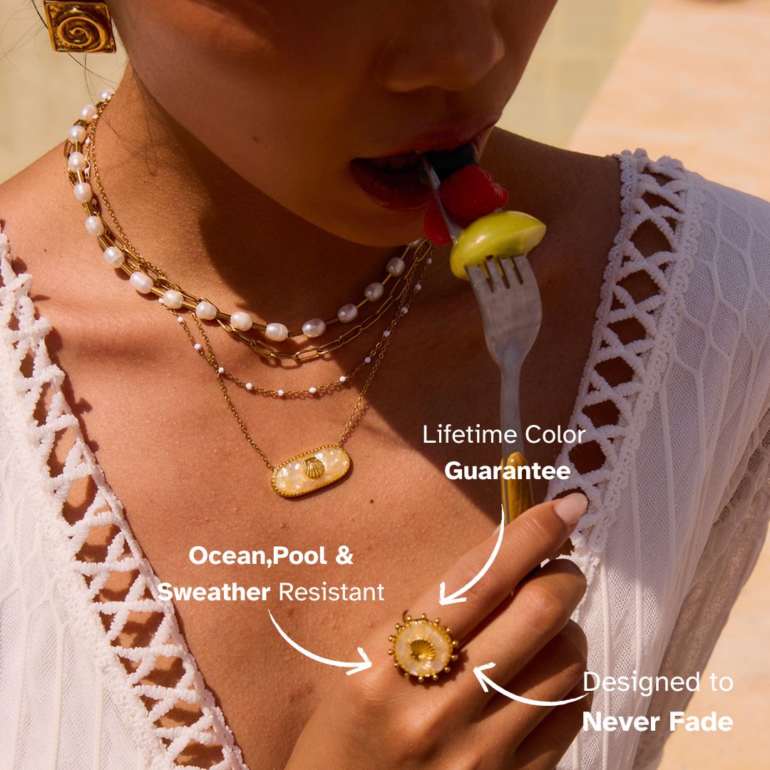 Sunlit close-up of model’s hand with golden seashell ring, tropical outdoor setting