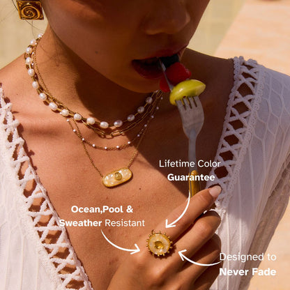 Sunlit close-up of model’s hand with golden seashell ring, tropical outdoor setting