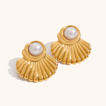 Close-up of golden shell pearl stud earrings on plain background.