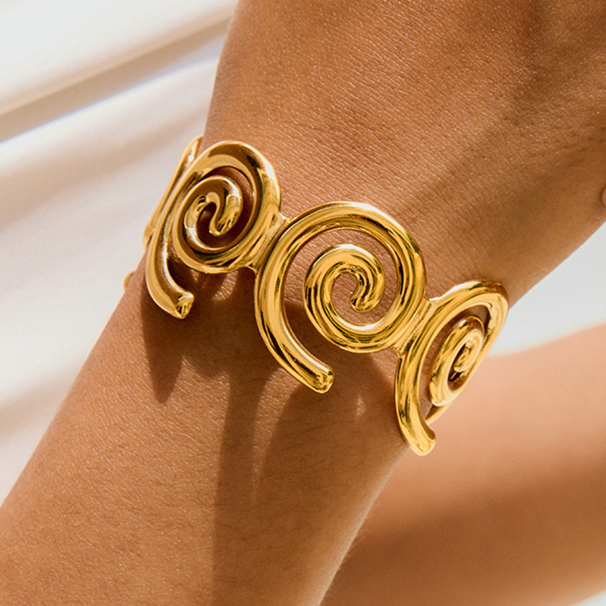 Gold swirl cuff bracelet with sculptural open design on model’s wrist outdoors