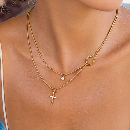 Gold necklaces with a cross pendant and another pendant on a person's neck.