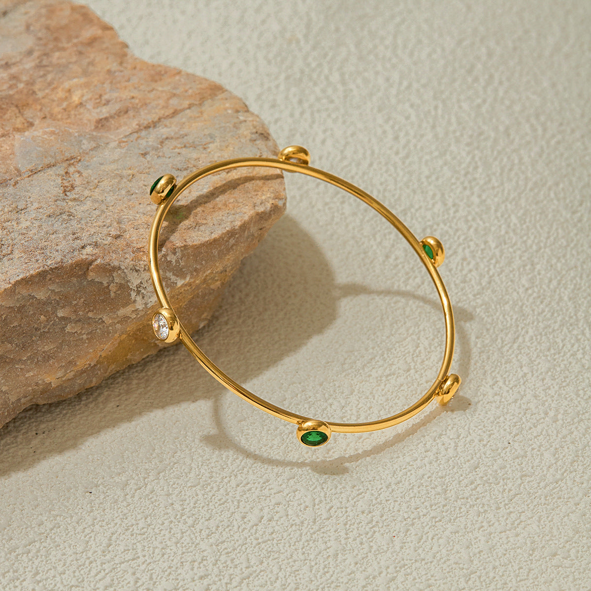 Green gem bangle with gold finish on stone background