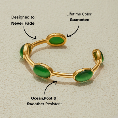 Gold cuff bracelet with oval green stones placed on a sandy surface