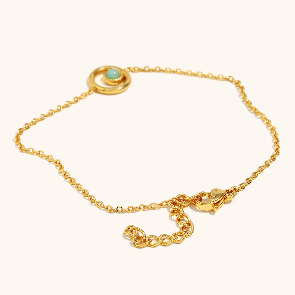Lightweight gold chain bracelet with double-ring charm and centered green stone.