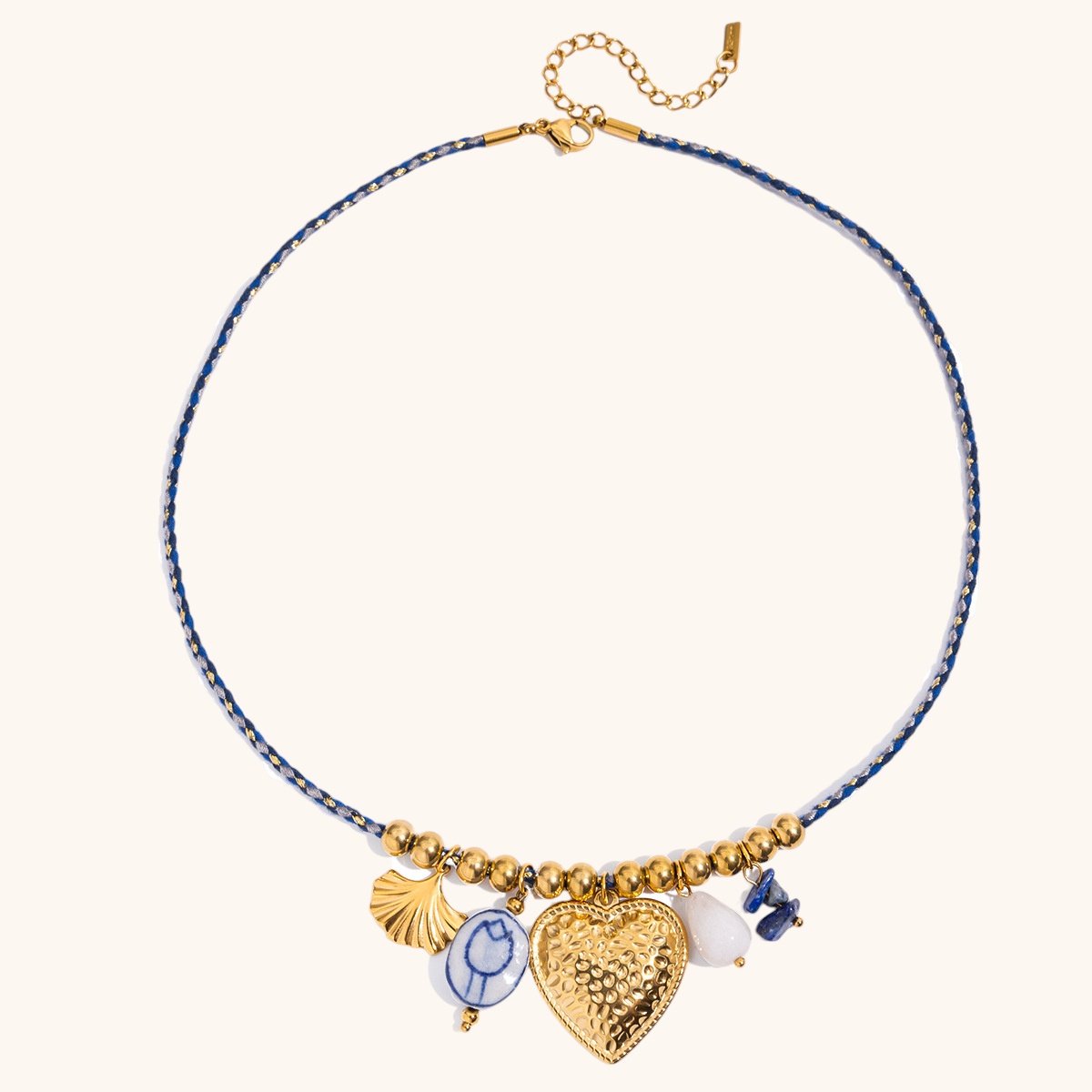 Close-up of gold heart charm necklace with blue ceramic and shell accents
