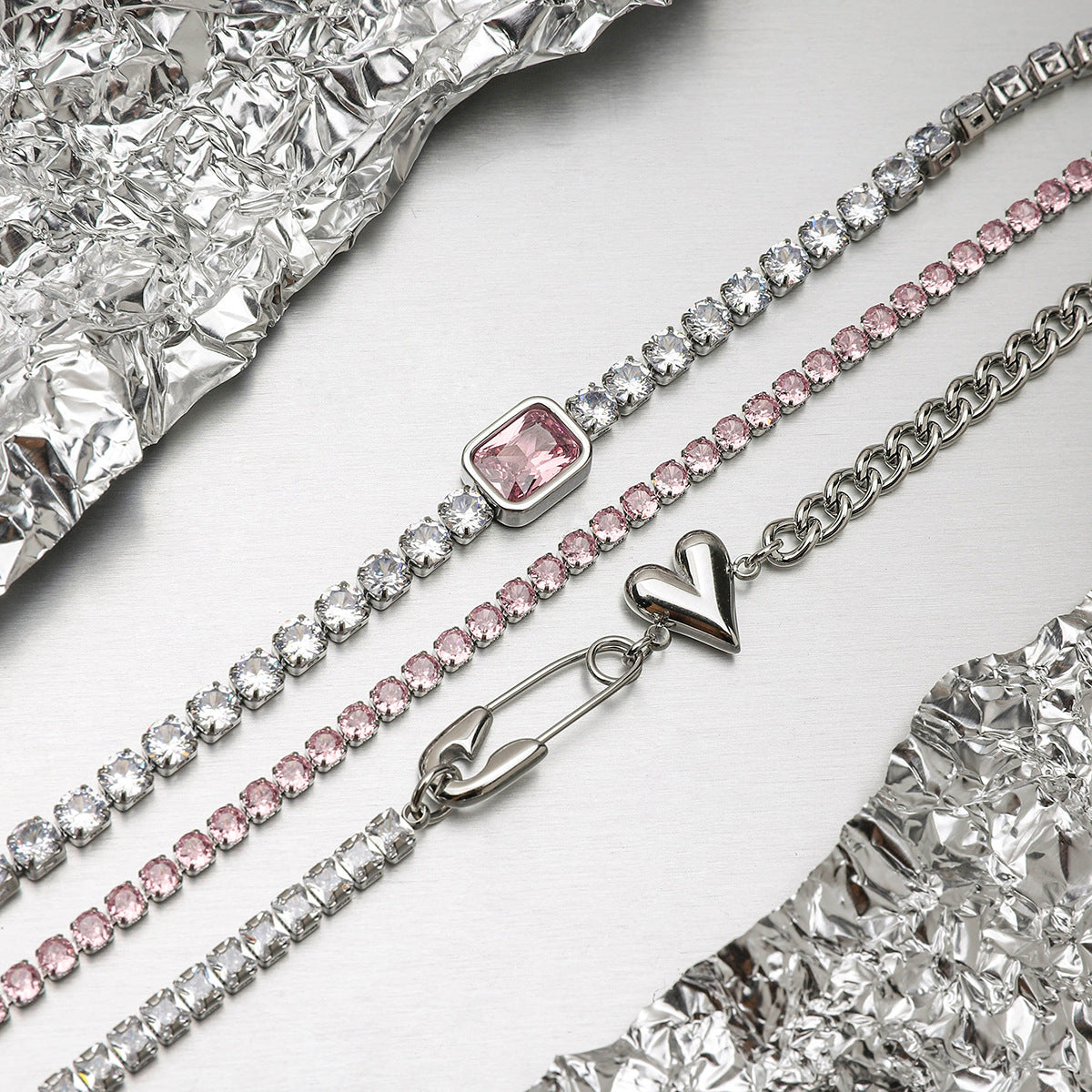 Trio of bracelets with silver heart, pink stones, and square crystal stacked for summer outfit.