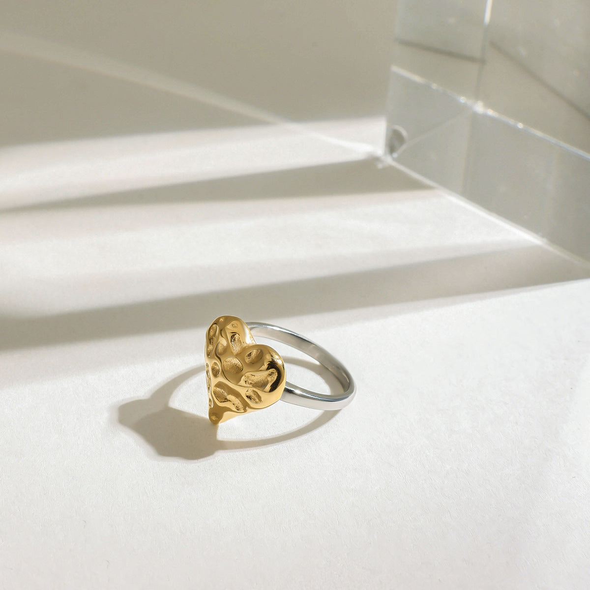 Textured heart ring and open heart ring styled on white surface with glass decor
