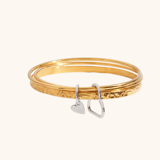 Three gold bangles with hammered finish and silver heart charm