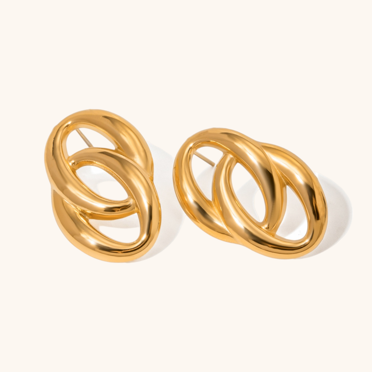 Studio image of high polish gold oval hoop earrings on cream background