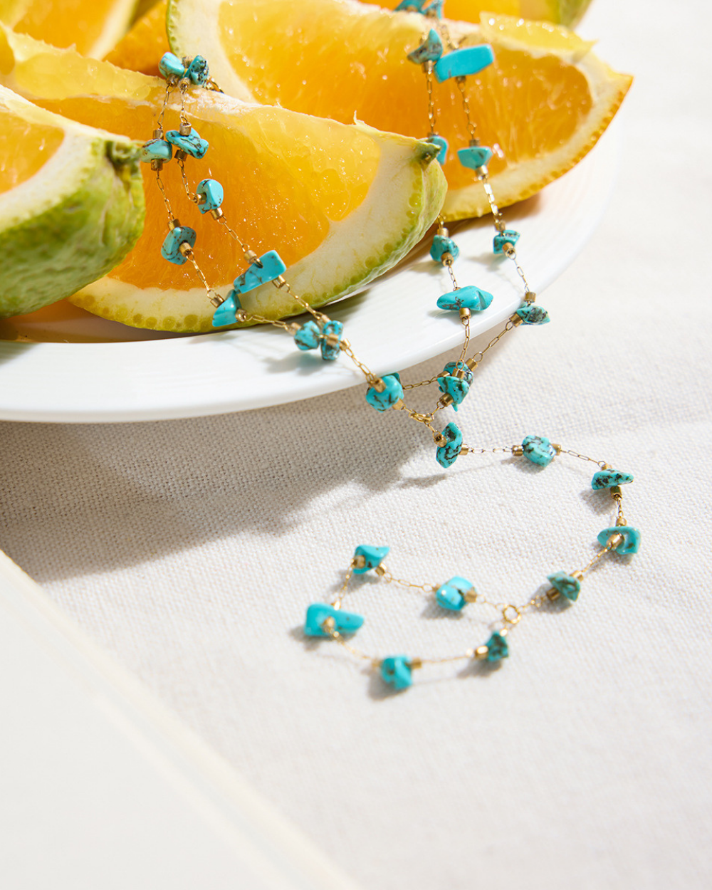 Necklace with turquoise beads on a white surface with orange slices