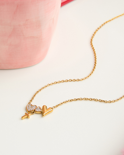 Gold necklace with heart and key pendant on a light pink background