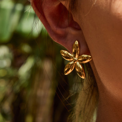 Model with slick hair wearing gold floral earrings in a tropical setting