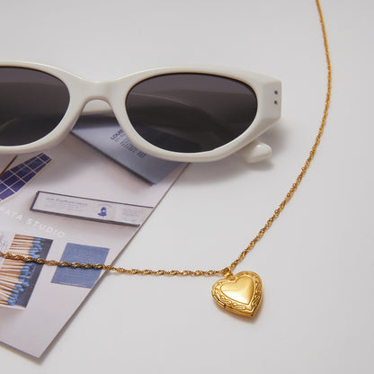Gold heart-shaped necklace with sunglasses on a light surface