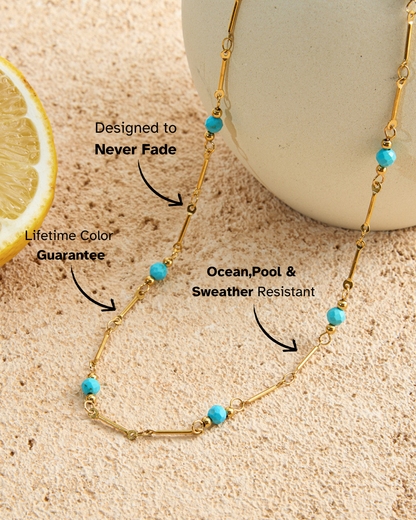 Gold necklace with blue beads on a sandy background, highlighting features like 'Designed to Never Fade' and 'Lifetime Color Guarantee'.