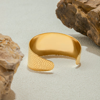 Gold bracelet with textured surface on a light gray background