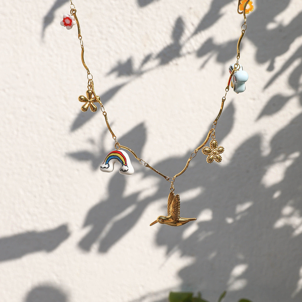 Woman wearing gold summer-themed charm necklace with colorful enamel pendants and floral earrings