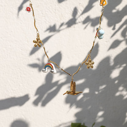Woman wearing gold summer-themed charm necklace with colorful enamel pendants and floral earrings