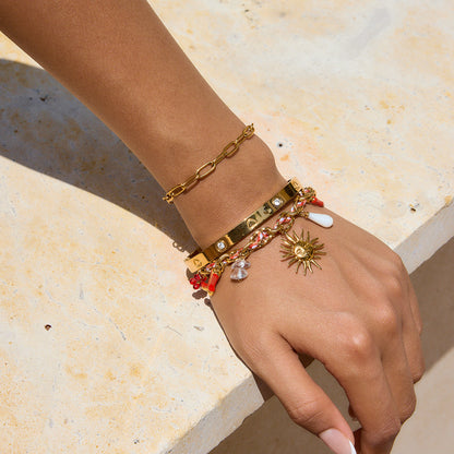 Hand wearing multiple gold bracelets with charms on a light stone surface