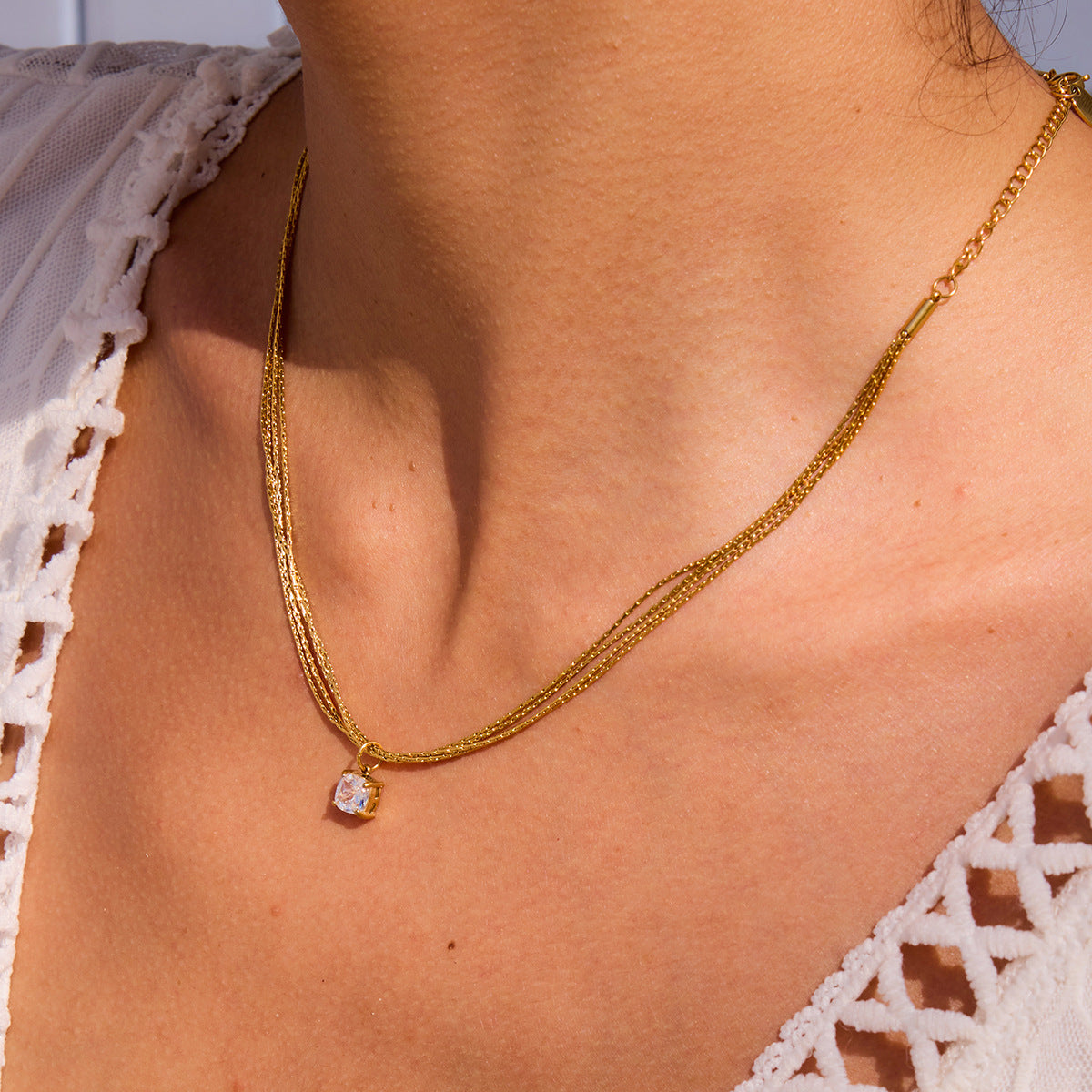 Model layering gold chain necklaces, featuring solitaire zircon pendant for summer look