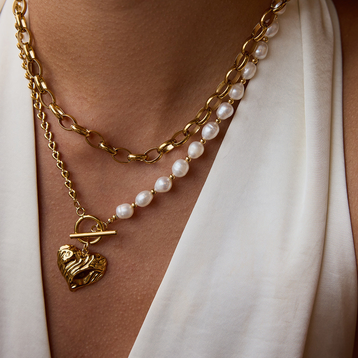 Model wearing layered gold and pearl necklace with textured heart charm, styled for a chic summer look