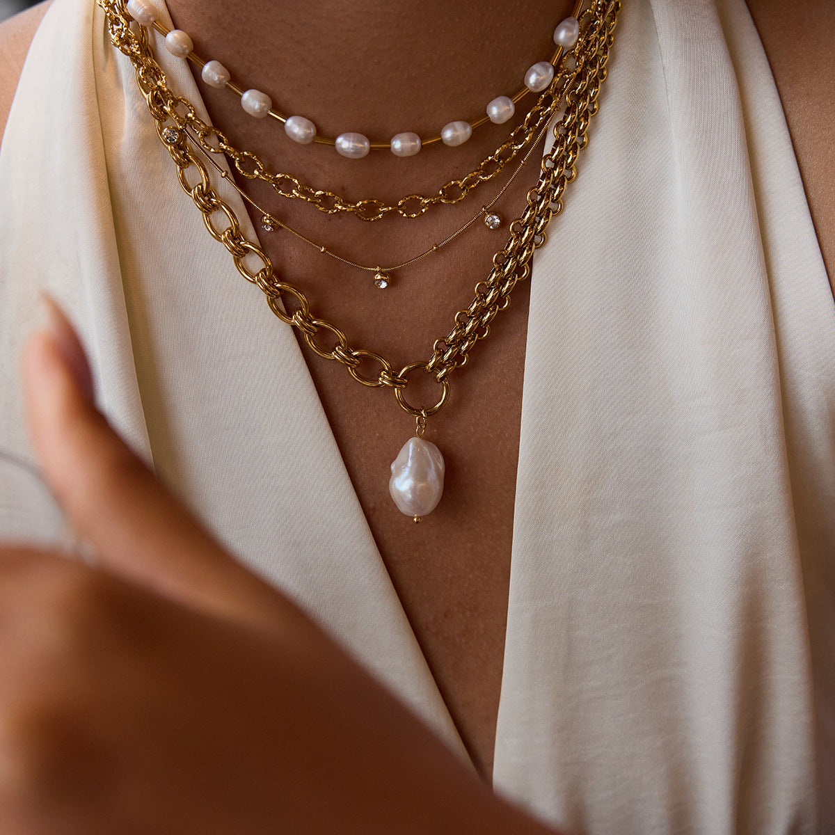 Stylish woman layering baroque pearl drop necklace with gold chains and pearls