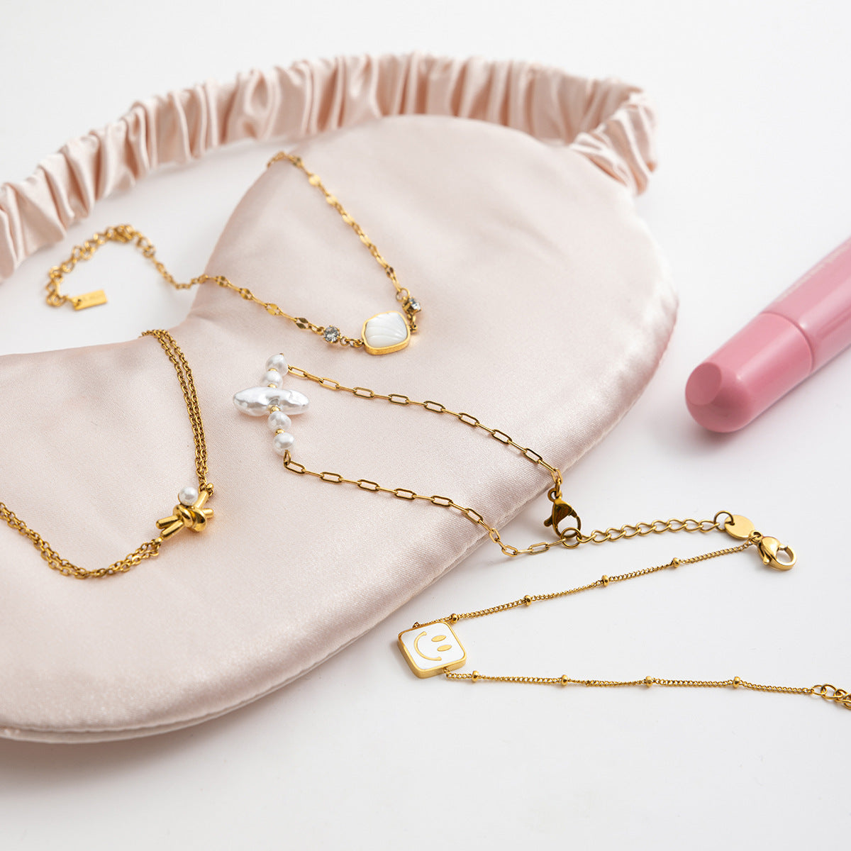 Gold necklaces on a pink jewelry pouch with a pink pen next to it.
