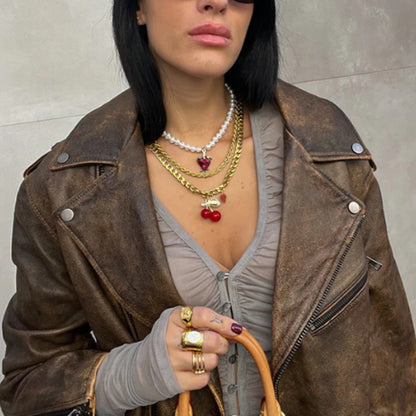 Woman wearing layered necklaces featuring a bold cherry pendant and vintage leather jacket