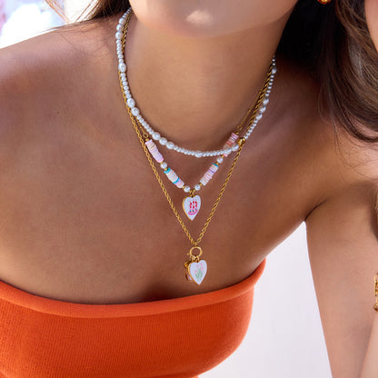 Model wearing layered heart pendant necklaces with pearls and pastel beads in a summer outfit
