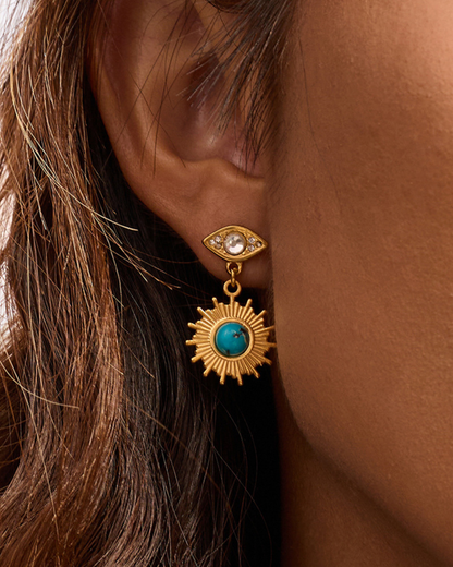 Close-up of a gold earring with a turquoise stone worn by a person.