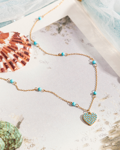 Necklace with heart pendant and turquoise beads on a textured surface with shells.