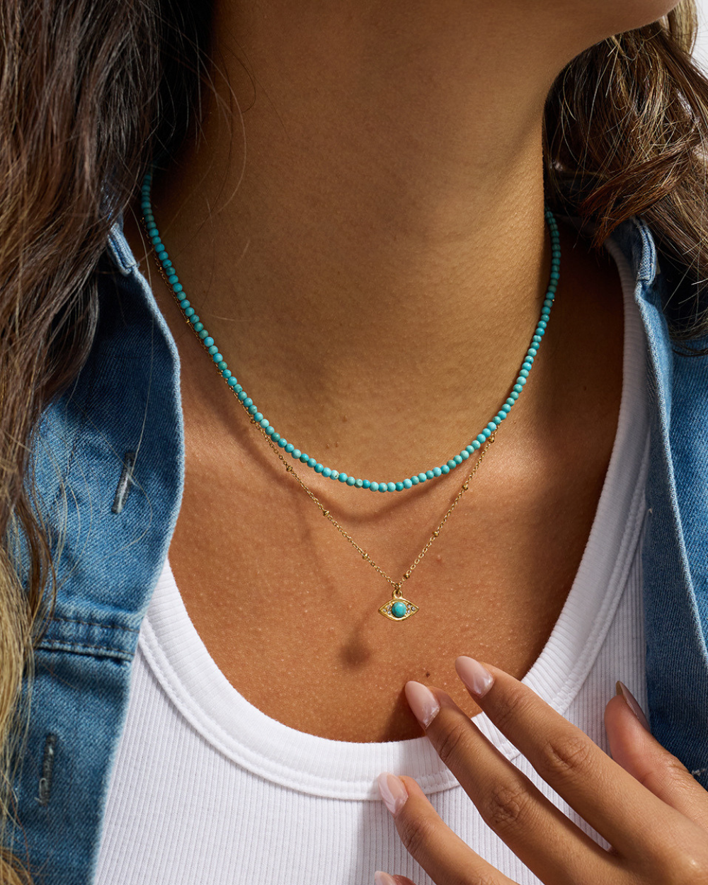 Close-up of a person wearing two necklaces with turquoise beads.