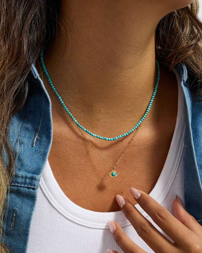 Close-up of a person wearing two necklaces with turquoise beads.
