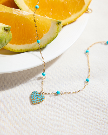 Necklace with heart-shaped pendant and turquoise beads on a white surface with orange slices in the background
