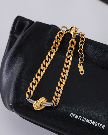 Gold chain bracelet on a black handbag with 'GENTLIOMONSTER' branding.