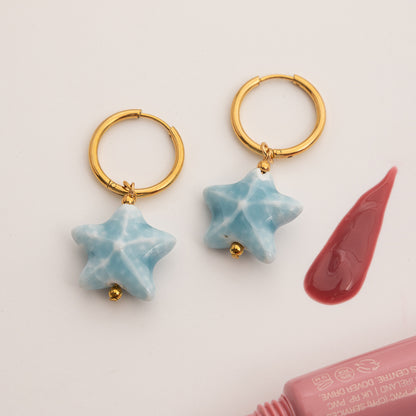 Gold hoop earrings with star-shaped blue charms on a light pink background