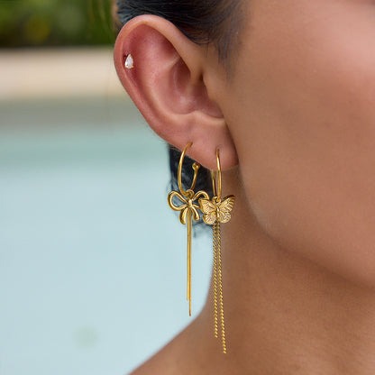 Model wearing layered gold earrings including butterfly dangle hoop