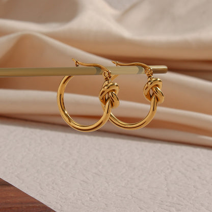 Ear detail showcasing knotted hoop earrings paired with small stud