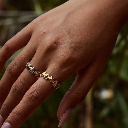 Two star rings (gold and mixed) styled together in an outdoor leafy background