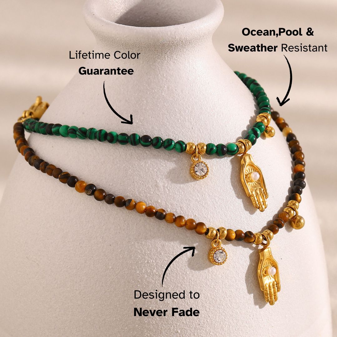 Close-up of green and brown beaded bracelets with hand and zircon charms on ceramic vase