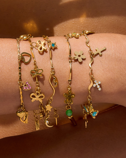 Gold bracelets with various charms on a wrist against a brown background