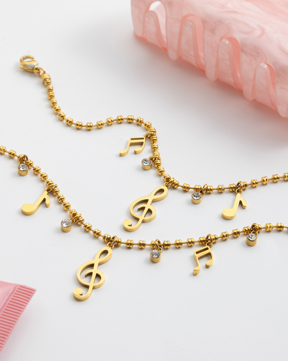 Gold necklace with musical sign charms on a light pink background