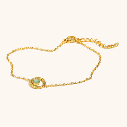 Close-up of dainty gold bracelet featuring a round green bead in orbit-style setting.