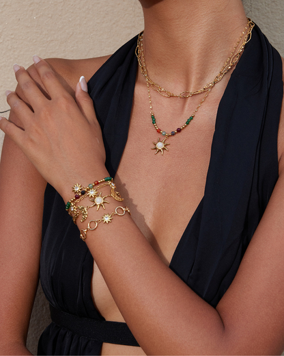 Gold jewelry set with necklace and bracelet on a person wearing a black top.