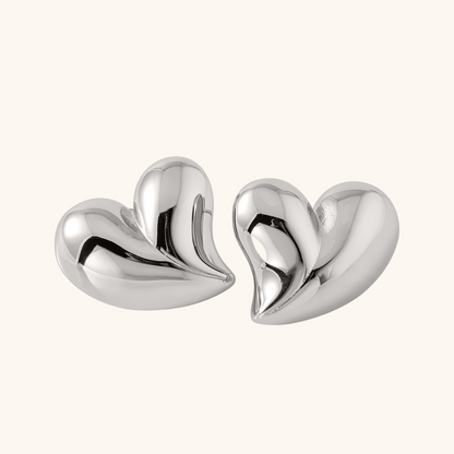 Simple silver heart earrings with reflective surface, soft light product display