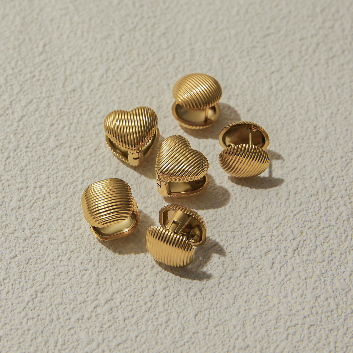 Multiple styles of ribbed earrings laid out on soft sand texture