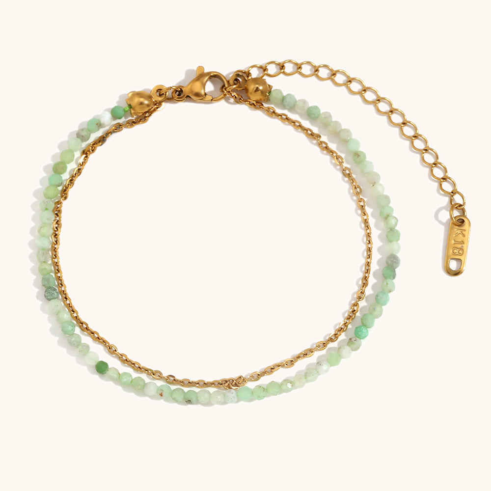 Gold-plated bracelet with light green beads and textured dual chain on stone backdrop.
