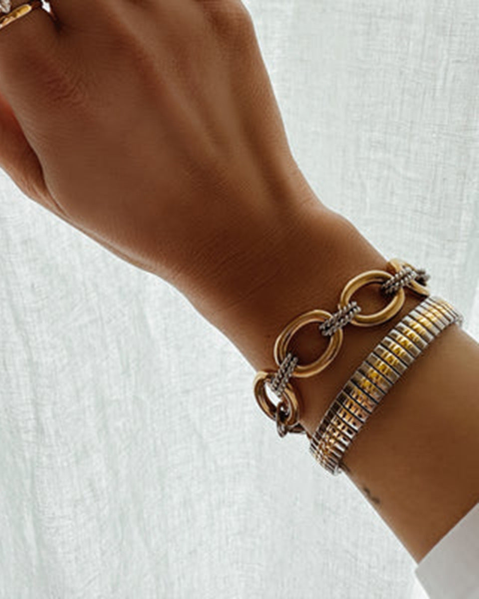 Close-up of a wrist wearing multiple gold and silver bracelets on a white background