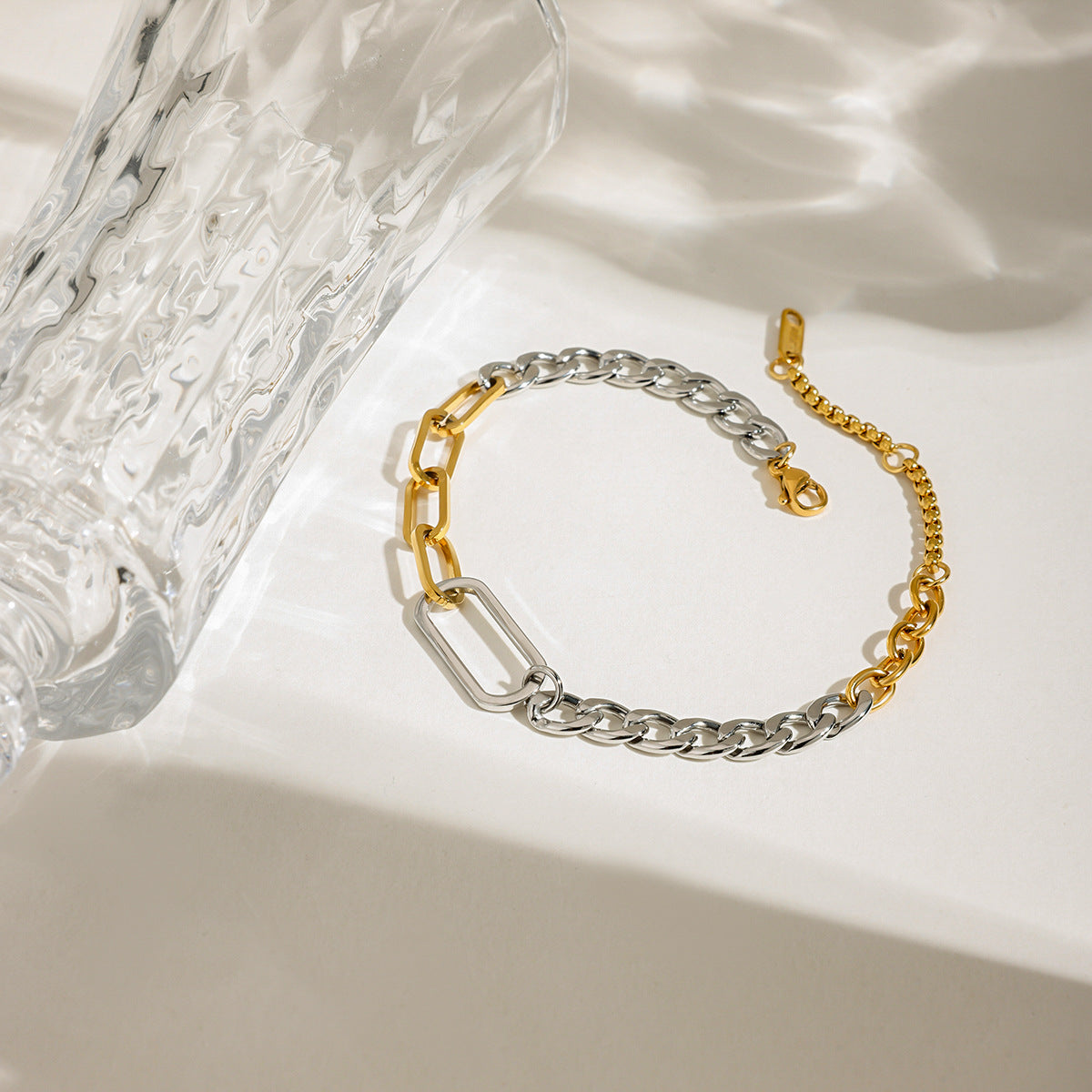 close-up of mixed gold and silver chain bracelet on white surface with crystal glass