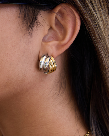Close-up of an ear wearing a gold and silver earring with a blurred background
