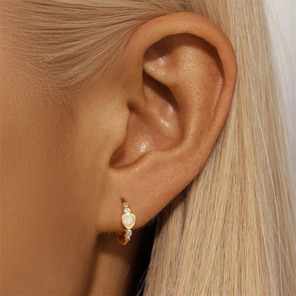 Model showcasing 14k gold-plated heart-shaped opal hoop earrings with zirconia accents, worn on the ear.